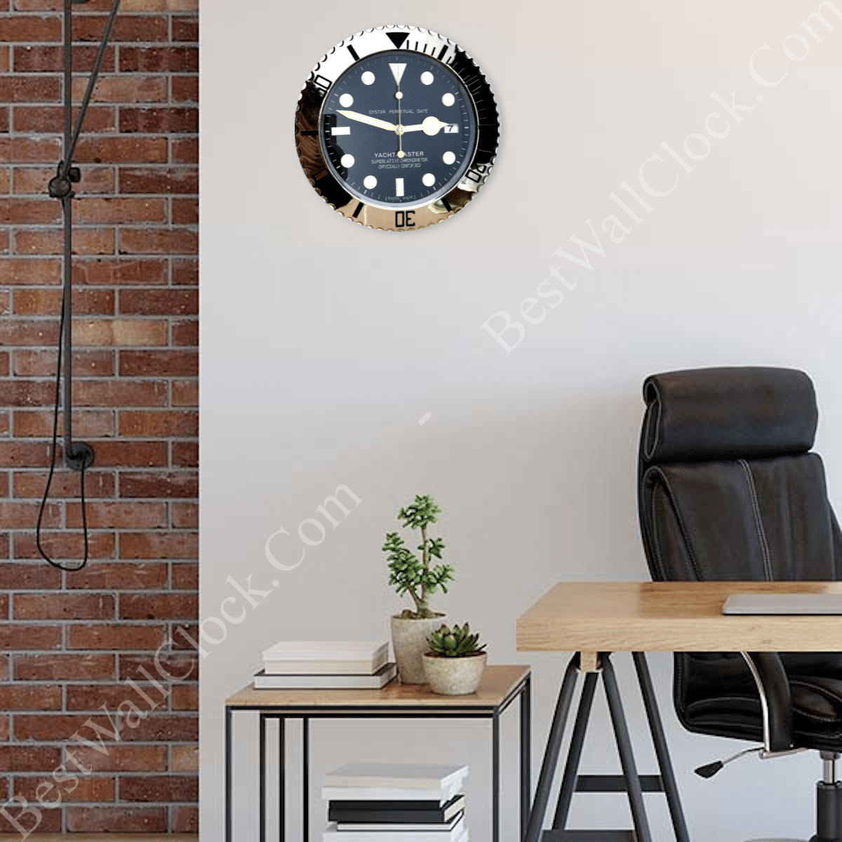 Modern office space with a wooden desk, black leather office chair, small wooden side table with potted plants and books, exposed brick wall on the left, and a round wall clock resembling a Rolex Yacht-Master watch on a plain light-coloured wall