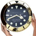 Two hands holding a large round wall clock designed like a Rolex Yacht-Master watch face with gold bezel and black dial showing the time as 8:14:44 with a date window displaying the number 16.