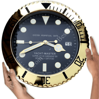 Two hands holding a large round wall clock designed like a Rolex Yacht-Master watch face with gold bezel and black dial showing the time as 8:14:44 with a date window displaying the number 16.