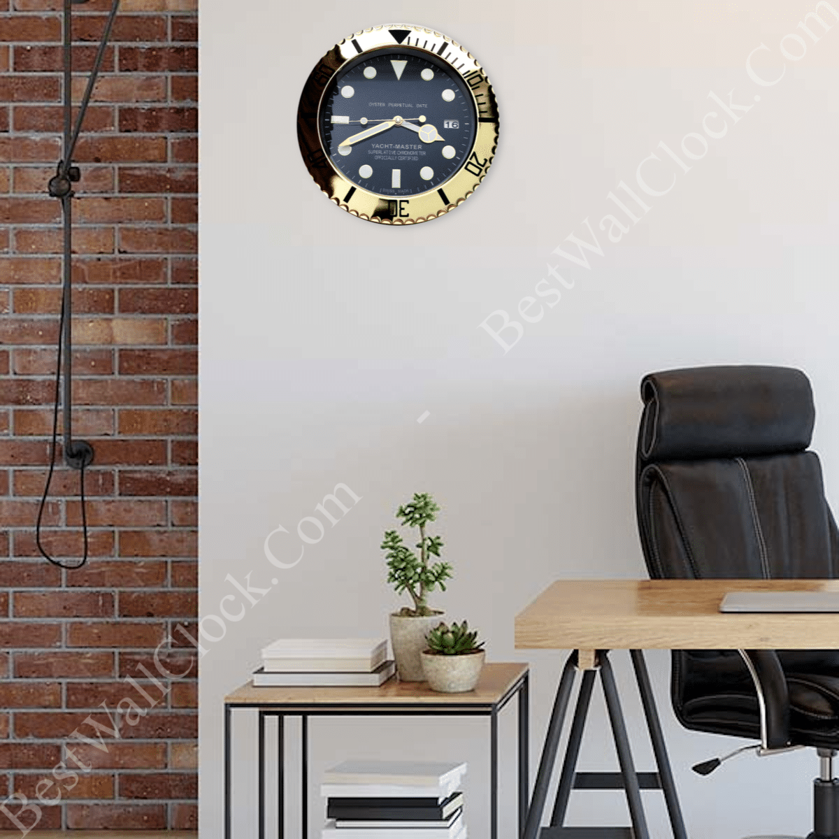 Modern office corner with a black ergonomic chair, wooden desk, small side table holding two potted plants and stacked books, and a wall clock designed to resemble a yacht master watch with gold and black bezel mounted on a plain white wall against a section of exposed red brick wall.