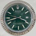 Close-up of a Rolex Oyster Perpetual Datejust watch face with a green patterned dial, silver hour markers and hands, a date window showing 16, and a fluted silver bezel.