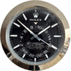 Round Rolex Sky-Dweller wristwatch face with black dial, silver hour markers and hands, displaying additional 24-hour time markings, encased in reflective silver bezel.
