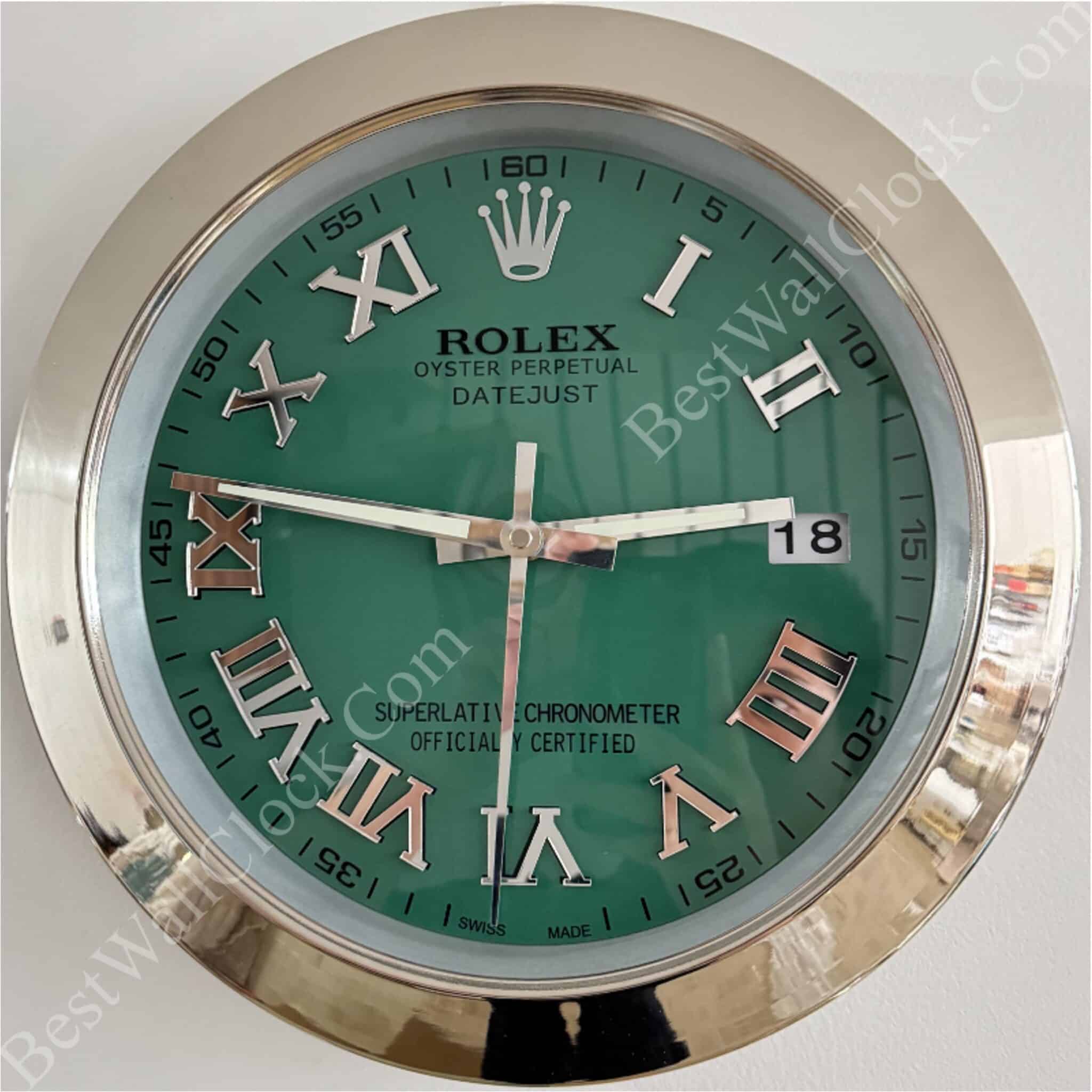 Round Rolex wall clock with green face, silver Roman numerals, silver frame, and date display showing 18, with hour hand near 3, minute hand near 9, and second hand near 6.