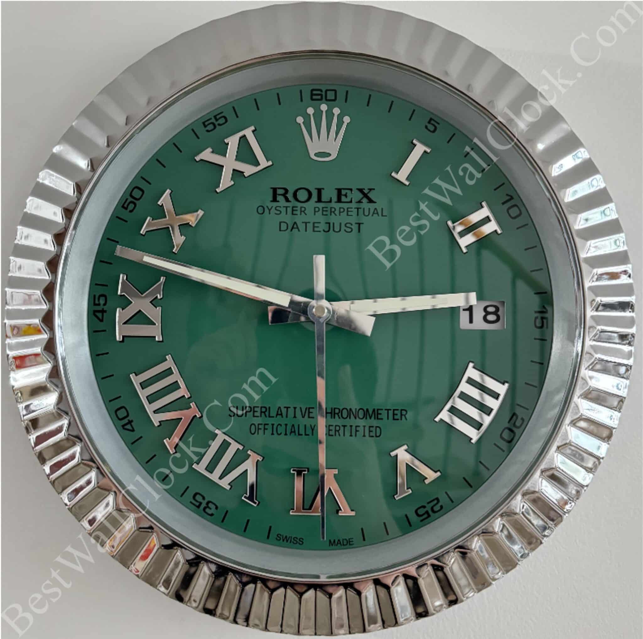 Round wall clock styled like a Rolex watch with a green face, silver Roman numerals, silver fluted frame, and the date showing 18