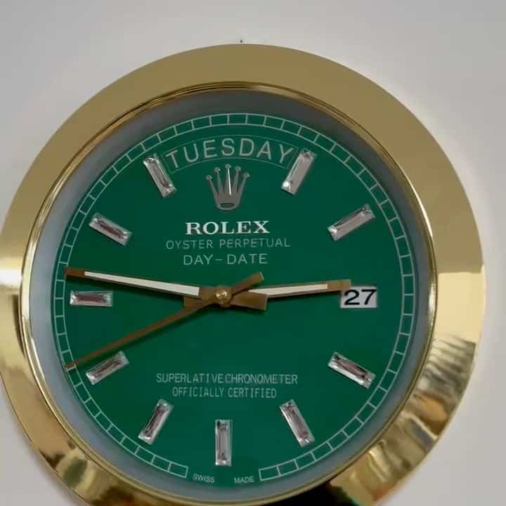 Close-up of a green Rolex Oyster Perpetual Day-Date clock with a gold rim, showing the day as Dinsdag and the date as 27, with silver hour markers and gold hands.