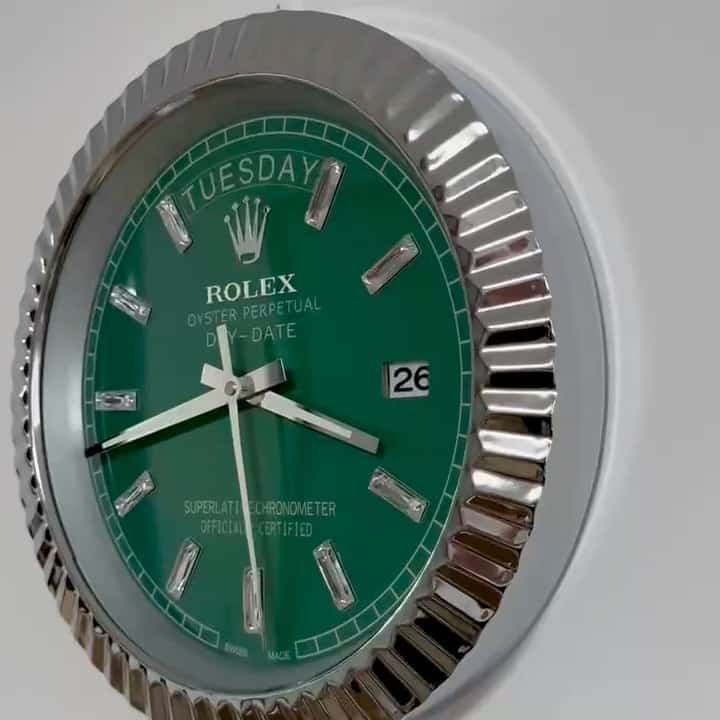 Close-up of a green Rolex Oyster Perpetual Day-Date wall clock with silver hour markers and a fluted silver bezel, showing the time as 9:15 and the date as the 26th on a white background.
