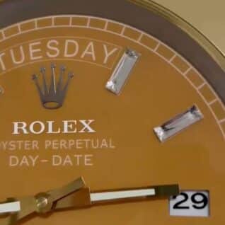 Close-up of a gold Rolex watch face showing the day Tuesday, diamond hour markers, and date 29 with gold and white hands.
