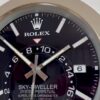 Close-up of a black Rolex Sky-Dweller watch face showing white hour markers, silver hands, a date window displaying the number 6, and text including the Rolex logo and model details.