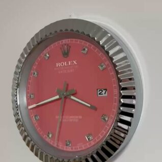 Close-up of a wall clock styled like a Rolex watch with a red face, silver rim, and diamond-like hour markers showing the time as 3:42:33 and the date as the 27th.