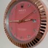Close-up of a Rolex Datejust watch face with a pink dial, diamond hour markers, gold hands, date window showing 27, and a fluted gold bezel.