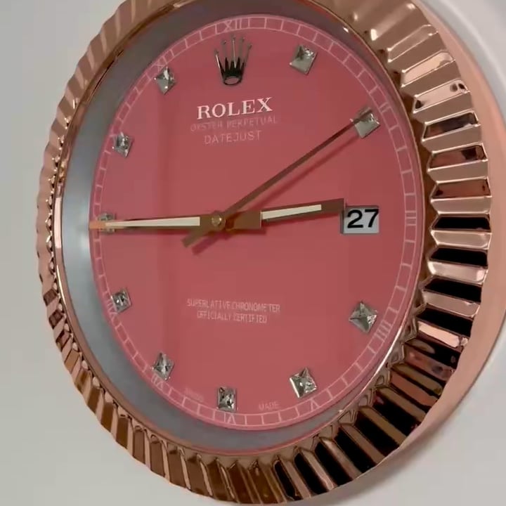 Close-up of a Rolex Datejust watch face with a pink dial, diamond hour markers, gold hands, date window showing 27, and a fluted gold bezel.