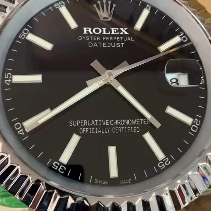 Close-up of a black Rolex Oyster Perpetual Datejust watch face with silver hour markers, silver hands showing 3:43, and a date display showing the number 8, with a silver fluted bezel.