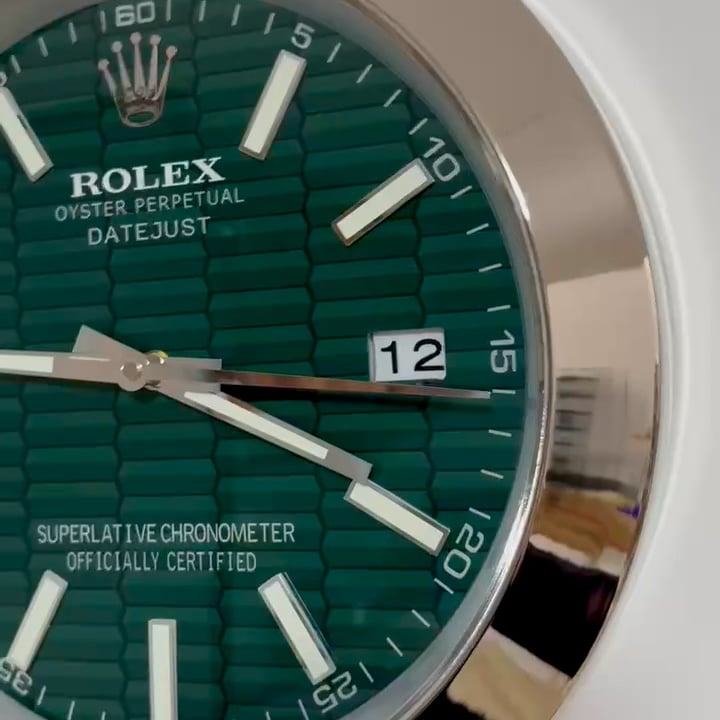 Close-up of a Rolex Oyster Perpetual Datejust watch face with a green textured dial, white rectangular hour markers, and a date window showing 12, with silver hands indicating the time as approximately 9:21.