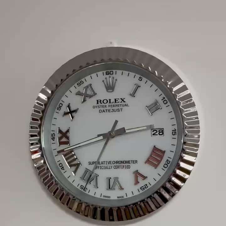 Rolex Oyster Perpetual Datejust wall clock with a white face, silver Roman numerals, date display at 3 o'clock, and a fluted metal bezel.