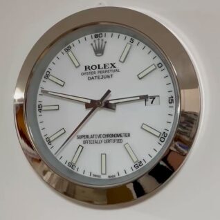 Close-up of a round wall clock designed like a Rolex Datejust watch face with a white dial, silver hour markers, and silver frame, showing the time as 3:47:37.