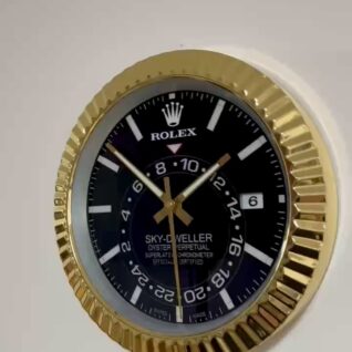 Close-up of a Rolex Sky-Dweller watch face with a gold fluted bezel, black dial, white hour markers, gold hands, and a date display showing '6'.