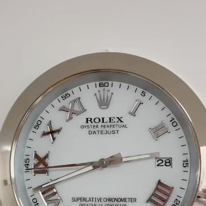 Close-up of a Rolex Oyster Perpetual Datejust watch face with Roman numerals and a date window showing 28, set against a light background.