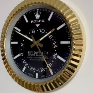 Close-up of a Rolex Sky-Dweller Oyster Perpetual wall clock with a black dial, gold fluted bezel, white hour markers, and three gold hands indicating the time.