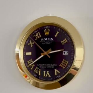 Gold-framed Rolex Oyster Perpetual Datejust wall clock with black face, gold Roman numerals, and a date window showing the 17th day, clock hands indicating 2:39:52.