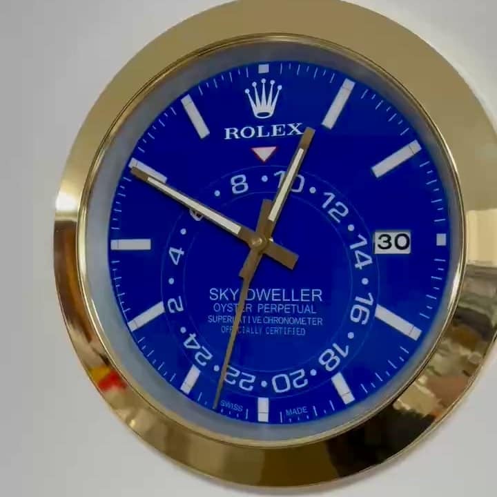 Close-up of a Rolex Sky-Dweller watch face with a blue dial, gold hands, white hour markers, and a date window showing the 30th, encased in a gold bezel.