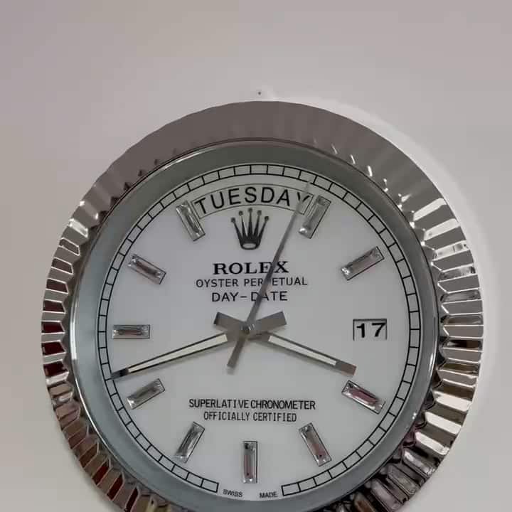 Close-up of a silver Rolex Oyster Perpetual Day-Date wall clock showing Salı the 17th, with a white face and silver hour markers on a ridged metallic frame.