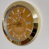 Close-up of a gold-framed Rolex Sky-Dweller wall clock with an orange dial showing the time 12:52:44 and displaying the date as the 6th.