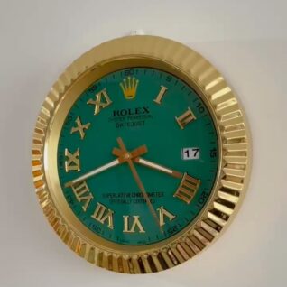 Wall clock styled like a Rolex Oyster Perpetual Datejust watch with a gold fluted bezel, green dial, gold Roman numerals, gold hands, and a date window showing 17, mounted on a white wall.