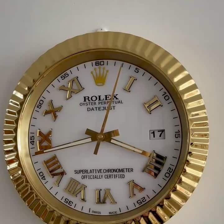 Close-up of a gold-framed Rolex Oyster Perpetual Datejust wall clock with white face, gold Roman numerals, and black minute markers showing the time as approximately 3:43:03 and the date as 17.