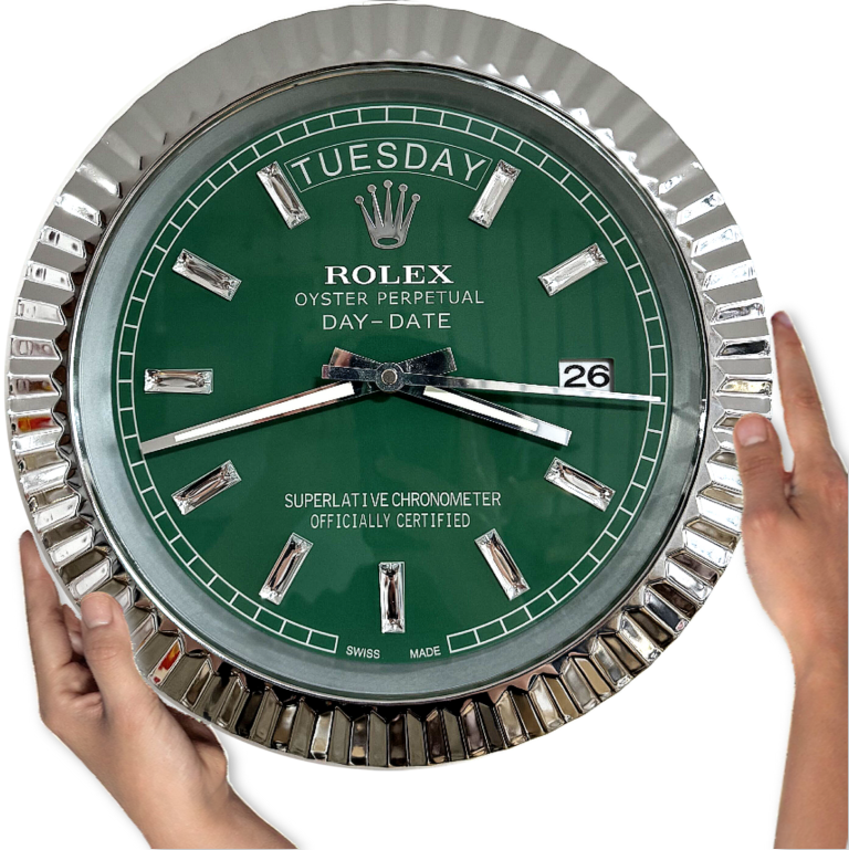 Hands holding a wall clock designed to resemble a Rolex Oyster Perpetual Day-Date watch with a green face, silver hour markers, and a date display showing terça-feira the 26th.
