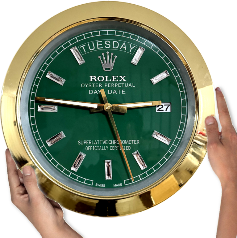 Hands holding a round Rolex wall clock with a green face, gold frame, and diamond-shaped hour markers, showing Dinsdag and the date 27 at 3 o'clock position.