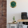 Modern office space with a wooden desk, black ergonomic chair, small side table holding stacked books and potted plants, light grey wall, exposed brick wall on the left, and a round gold-framed Rolex wall clock showing Dinsdag the 27th.
