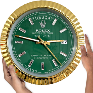 Hands holding a large Rolex clock with a gold fluted bezel, green dial displaying the day 'Tuesday' at 12 o'clock and date '27' at 3 o'clock, with gold hour, minute, and second hands and rectangular hour markers.