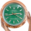 Hand holding a large Rolex Oyster Perpetual Day-Date wall clock with a green face, gold accents, and displaying Tuesday the 26th