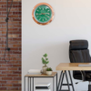 Modern office interior with a green and rose gold Rolex wall clock showing Tuesday 26, a wooden desk with a black office chair, a small table with potted plants and stacked books, and a brick accent wall on the left.