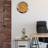 Modern office interior with a wooden desk, black leather office chair, small side table with potted plants and books, exposed brick wall on the left, and a wall clock with an orange Rolex Day-Date dial mounted on a plain light-colored wall.