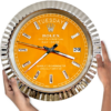 Hands holding a large Rolex wall clock with an orange face, silver hour markers, and a fluted silver bezel, displaying tirsdag 29th and the time as 7:21:44.