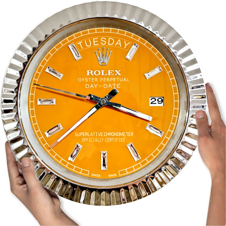 Hands holding a large Rolex wall clock with an orange face, silver hour markers, and a fluted silver bezel, displaying tirsdag 29th and the time as 7:21:44.
