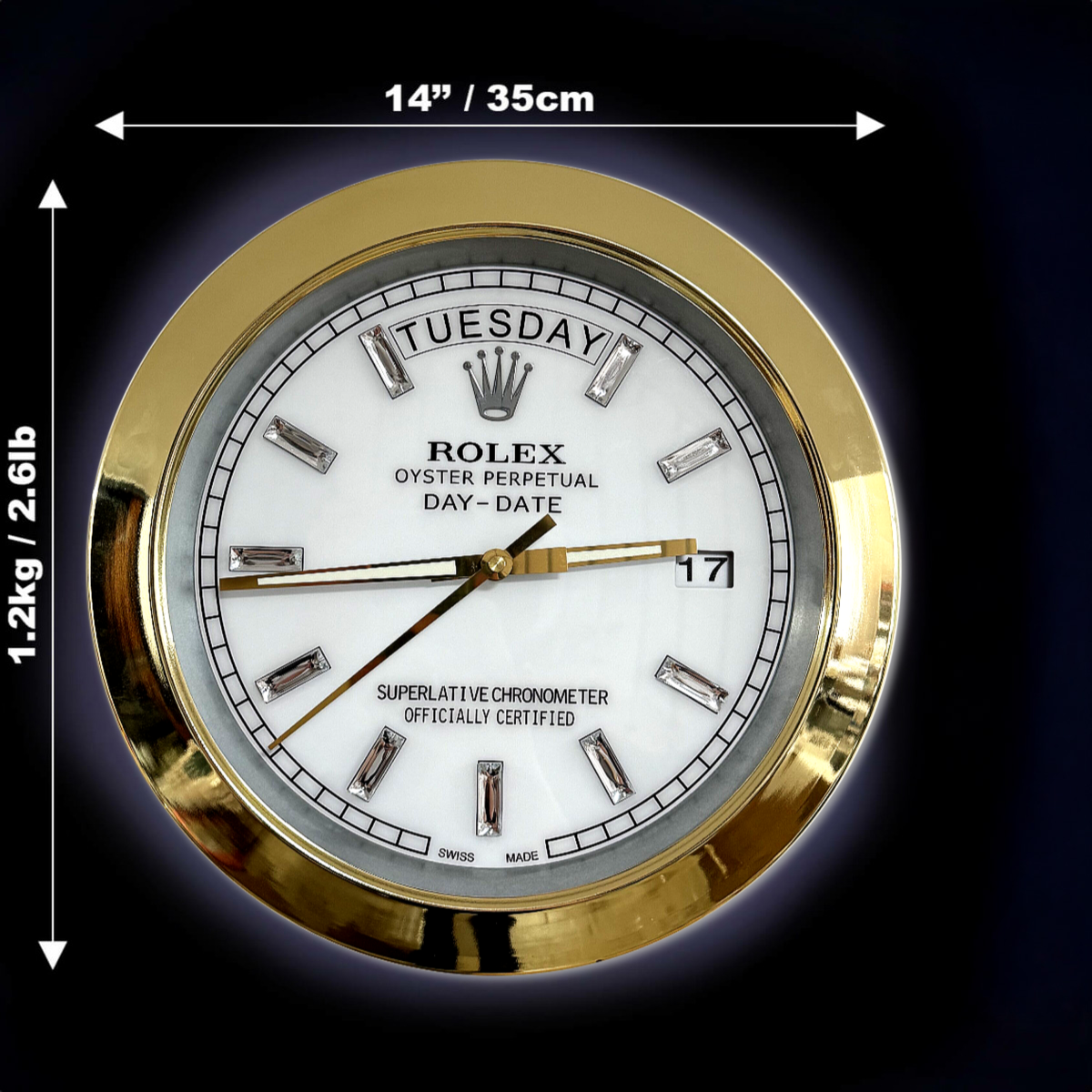 Round gold-framed Rolex Oyster Perpetual Day-Date wall clock with white face, diamond hour markers, displaying Dinsdag as the day and 17 as the date, with dimensions 14 inches (35 cm) diameter and weight 1.2 kg (2.61 lb) indicated by white arrows on a black background.