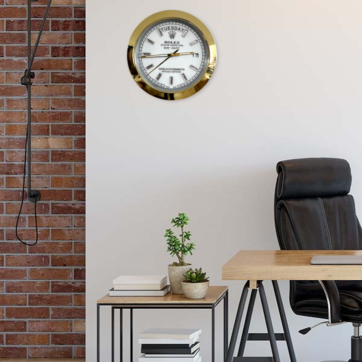 Modern office interior with a wooden desk, black leather office chair, side table with potted plants and books, brick wall on the left, and a gold-framed wall clock showing Dinsdag 9:15 on a white wall.
