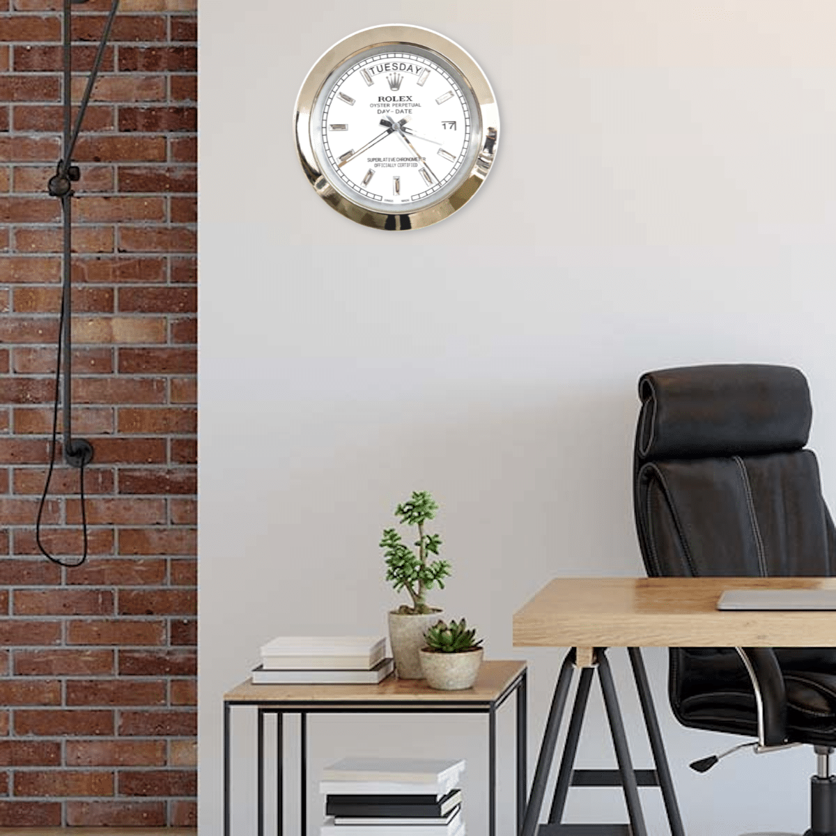 Modern office corner with a black leather chair, wooden desk, and two small potted plants on a stackable side table, with a white and gold Rolex wall clock showing Martedì and time around 5:11 on a plain light wall next to an exposed red brick wall.