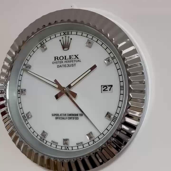 Close-up of a Rolex Oyster Perpetual Datejust wall clock with a fluted silver frame, white dial, diamond hour markers, Roman numerals at quarter hours, and a date display showing 27.