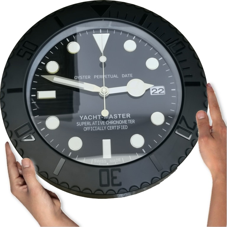 Black Yacht-Master wall clock with white markers and date window showing 22, held by two hands on either side